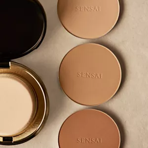 Total Finish foundation compact case and sponge next to three refill shades on neutral surface